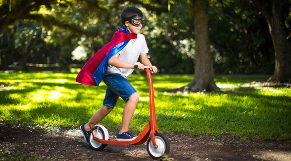 Boy in superhero costume riding scooter